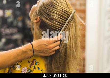 Main de coiffeur de sexe masculin peignant les cheveux blonds longs d'une femme . Photo de haute qualité Banque D'Images