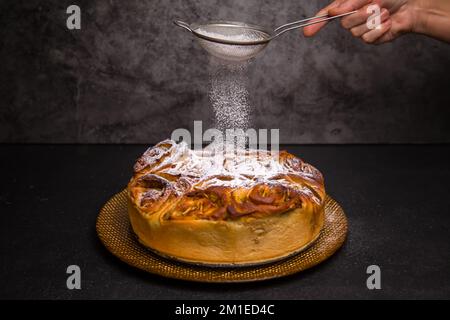 Tarte aux pommes. Sucre en poudre. Arrière-plan sombre. La tarte aux pommes juste en dehors du four est arrosée de poudre de sucre Banque D'Images