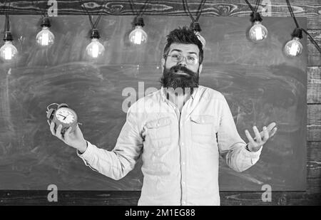 Concept de calendrier et de régime. Homme à la barbe et à la moustache sur l'expression du visage confuse en classe. L'hipster barbu tient l'horloge et le tableau Banque D'Images