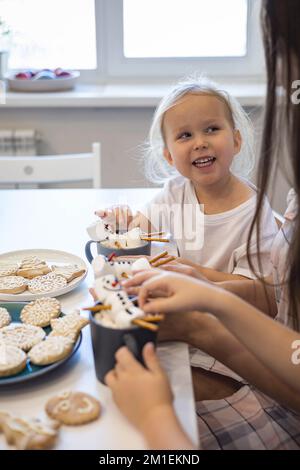 Les parents et les enfants font des bonshommes de neige à partir de guimauves. Ils boivent du cacao et se préparent pour Noël. Concept de la maison de Noël. Banque D'Images