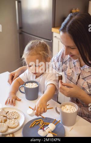 Les parents et les enfants font des bonshommes de neige à partir de guimauves. Ils boivent du cacao et se préparent pour Noël. Concept de la maison de Noël. Banque D'Images