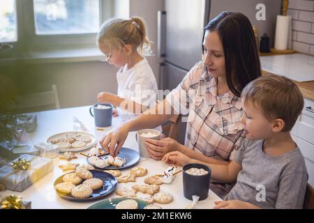 Les parents et les enfants font des bonshommes de neige à partir de guimauves. Ils boivent du cacao et se préparent pour Noël. Concept de la maison de Noël. Banque D'Images