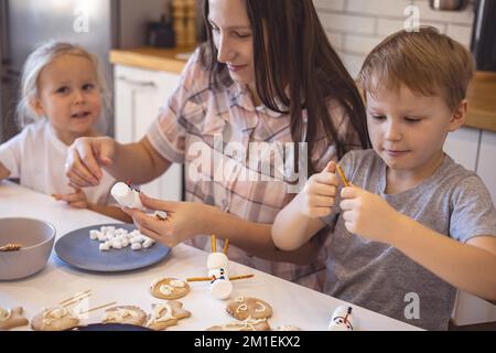 Les parents et les enfants font des bonshommes de neige à partir de guimauves. Ils boivent du cacao et se préparent pour Noël. Concept de la maison de Noël. Banque D'Images