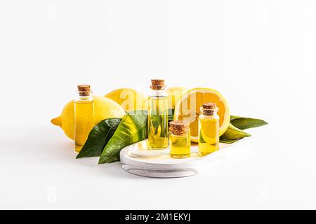 un ensemble de bouteilles de verre avec un liège avec un remède de citron biologique, essence, huile sur un plateau de plâtre blanc parmi les fruits mûrs. arrière-plan blanc. vue avant Banque D'Images