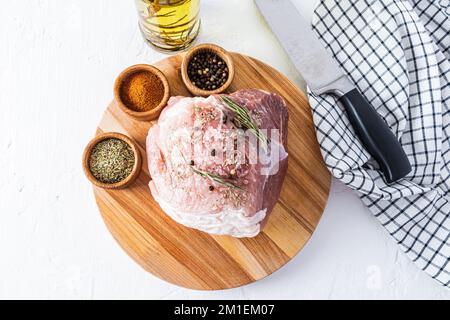 un grand morceau de porc frais pour la cuisson repose sur une planche ronde en bois avec diverses épices. vue de dessus. arrière-plan blanc Banque D'Images