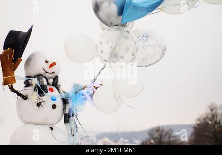 Bonhomme de neige en chapeau, foulard, gants avec ballons d'air vous souhaite Joyeux Noël. Vacances d'hiver. Banque D'Images