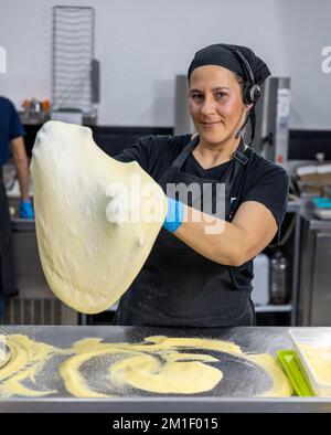 Femme chef professionnelle étire et roule la pâte pour pizza Banque D'Images