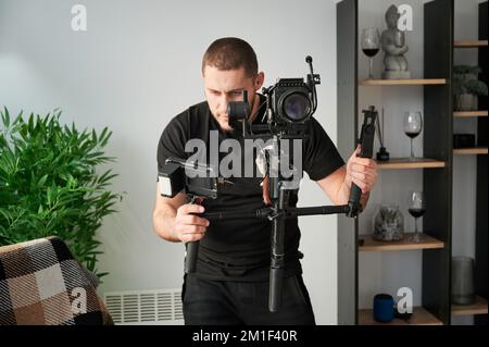 Vidéaste homme filmant en intérieur, à l'aide d'une caméra montée sur un stabilisateur de nacelle. Banque D'Images