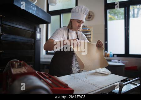 Boulanger jeune avec chapeau de chef préparant des pâtisseries dans la boulangerie. Banque D'Images