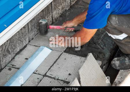 Couche de briques professionnelle pour la pose de carreaux. Les mains du constructeur en gros plan avec un marteau. Réparation d'échafaudages en pierre de bâtiments. Entrepreneur en construction en travaux. Flux de travail réel... Banque D'Images