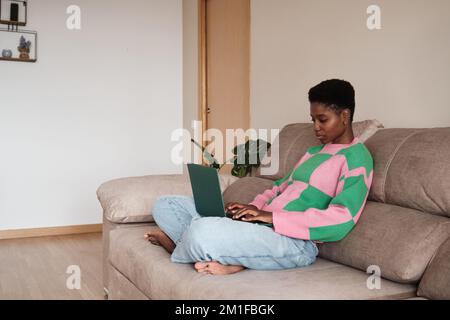 Femme indépendante noire utilisant un ordinateur portable tout en étant assise sur un canapé Banque D'Images