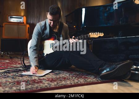 prise de vue complète d'un jeune guitariste assis sur le sol avec une guitare basse et des notes écrites dans le studio. Photo de haute qualité Banque D'Images