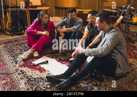 les membres du groupe moderne sur le sol parlent, le microphone est en face d'eux sur le sol, studio d'enregistrement. Photo de haute qualité Banque D'Images