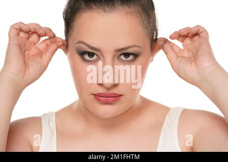 Une femme malheureuse qui tire ses oreilles avec ses doigts sur fond blanc. Banque D'Images