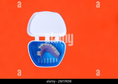 réservoir à prothèse ouverte à charnière blanche avec fausses dents isolées sur fond orange Banque D'Images