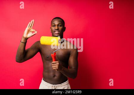 Un peintre africain s'est concentré sur le travail tenant un rouleau professionnel pour peindre un mur intérieur, studio. Banque D'Images