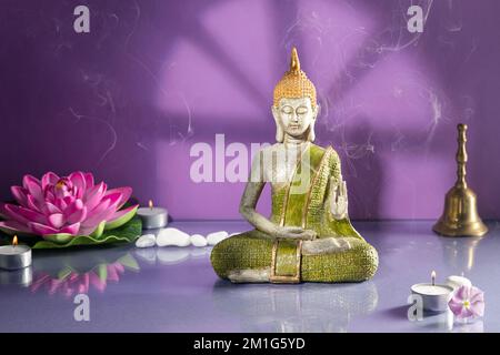 Statue de bouddha verte et dorée en méditation sur fond violet clair avec espace de copie. Banque D'Images
