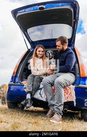 Un homme avec une femme s'amuse avec son chien en plein air dans la forêt près de la voiture. Banque D'Images