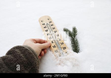 Gros plan de la main des femmes dans un sweat-shirt en polaire contenant un thermomètre indiquant une température en degrés Celsius en dessous de zéro.hiver gel. Branche d'épinette dans Banque D'Images