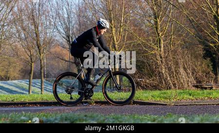 Homme habillé en Lycra noir à cheval sur un Moda vélo sur un froid, lumineux, hiver matin Banque D'Images