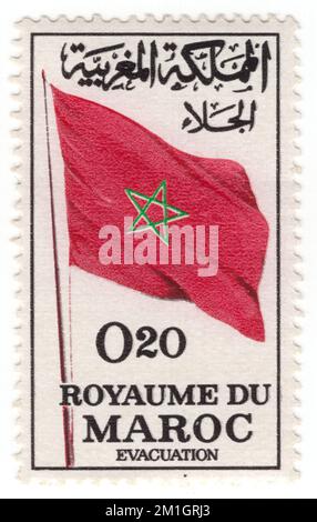 MAROC - 1964 25 décembre : un timbre noir de 20 centimes, un carmin profond et un timbre-poste vert représentant le drapeau marocain. Évacuation de toutes les forces militaires étrangères du territoire marocain. Le drapeau du Maroc est le drapeau utilisé par le gouvernement du Maroc qui a servi de drapeau national du Maroc depuis le 17 novembre 1915. C'est un champ rouge avec une étoile verte au centre. L'étoile verte représente les cinq piliers de l'Islam et le rouge représente le sang des ancêtres et l'unité. Red a une importance historique considérable au Maroc, proclamant la descente de la dynastie royale Alawid Banque D'Images