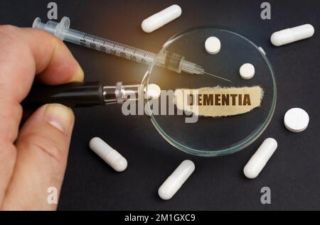 Un homme regarde à travers une loupe sur les pilules, une seringue et un morceau de papier avec l'inscription DÉMENCE Banque D'Images