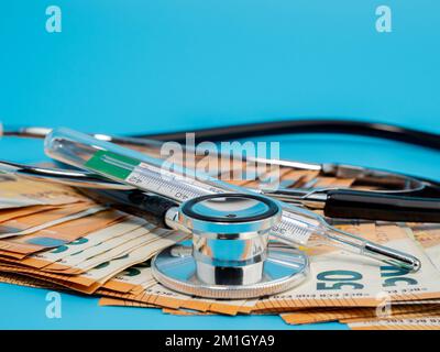 Stéthoscope médical, thermomètre et billets sur fond bleu. Gros plan. Banque D'Images