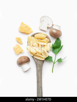 Pâtes crues aux champignons et au parmesan dans une cuillère en bois sur fond blanc Banque D'Images