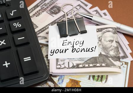 Concept financier et commercial. Sur fond marron se trouve une calculatrice et des dollars sur un clip avec une inscription sur papier - Profitez de votre bonus Banque D'Images