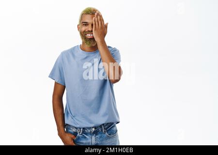 Beau Noir homme couvre la moitié de son visage, avant et après concept, vérifie ses yeux à l'opticien, se tient sur fond blanc Banque D'Images