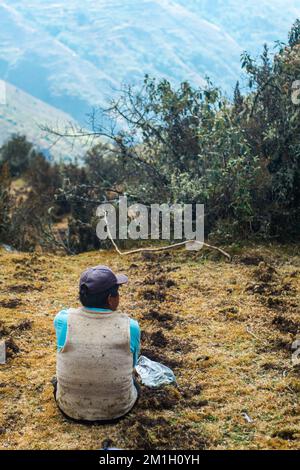 Vue arrière verticale d'un agriculteur péruvien assis en regardant sur le paysage des Andes péruviennes Banque D'Images