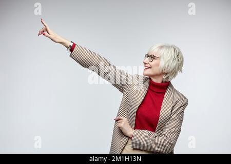 belle femme âgée avec des verres points avec son index à un siège vide. concept publicitaire d'une femme d'affaires leader. Banque D'Images