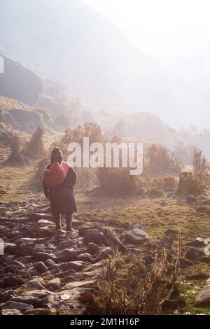 Un dos vertical d'une agricultrice des Andes péruviennes transportant de la nourriture enveloppée dans une couverture Banque D'Images