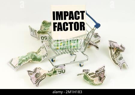 Concept d'affaires et d'économie. Les dollars froissés se trouvent sur une surface blanche, il y a un chariot à l'intérieur d'un panneau avec l'inscription - FACTEUR D'IMPACT Banque D'Images