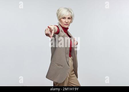 belle femme âgée avec des lunettes pointe son doigt vers l'appareil photo. le concept d'une femme d'affaires leader. Banque D'Images