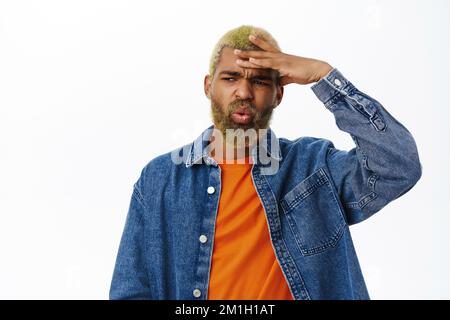 Portrait de l'homme de style afro-américain, semble choqué, touche sa tête et fixe en incrédulité à l'appareil photo, se tient sur fond blanc Banque D'Images