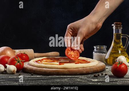 Le processus de fabrication de pizza. La main d'un homme met une tomate sur une pizza. Banque D'Images