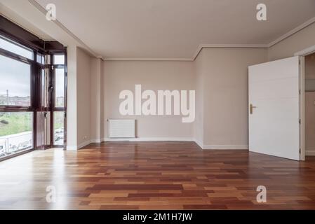 Un salon avec parquet rougeâtre, une fenêtre en aluminium anodisé rouge foncé et boiseries blanches Banque D'Images