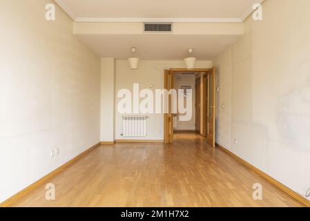 Une chambre vide avec deux portes en bois, un radiateur en aluminium, la climatisation à travers des conduits cachés dans le faux plafond et parquet en chêne. Banque D'Images