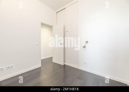 Cette chambre vide présente des murs blancs lisses, une armoire intégrée du sol au plafond dotée de portes coulissantes et de parquet gris Banque D'Images