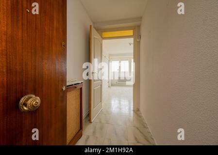 Hall d'entrée d'une maison avec une porte d'accès en bois massif, un petit couloir, des sols carrelés de véine blanche et un couvercle de radiateur avec grilles Banque D'Images