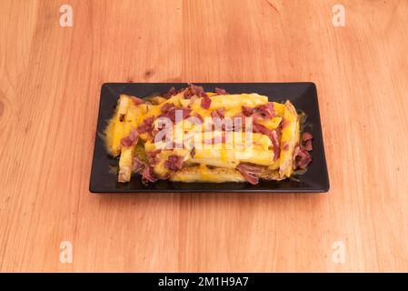 une portion de frites avec beaucoup de fromage fondu et du bacon sur une table en bois Banque D'Images