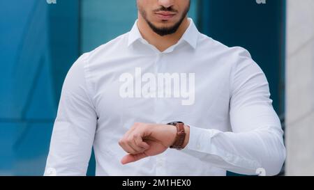 Inreconnaissable arabe hispanique homme d'affaires avec barbe jeune patron responsable porte blanc chemise classique regarde la montre de poignet en colère de l'heure tardive Banque D'Images