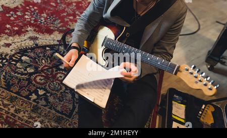 plan court d'un guitariste tenant des feuilles de notes et assis sur le sol. Photo de haute qualité Banque D'Images