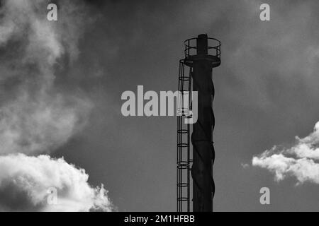 Un cliché en échelle de gris d'une cheminée industrielle avec un ciel nuageux en arrière-plan Banque D'Images