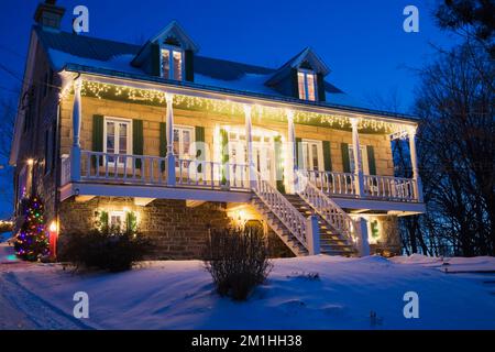 Ancienne maison de style cottage Canadiana 1870 illuminée de lumières de Noël la nuit en hiver. Banque D'Images