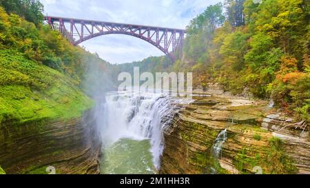 Pont de marron d'acier au-dessus d'une superbe cascade qui fait rage et qui traverse des falaises superposées dans une forêt verdoyante luxuriante Banque D'Images