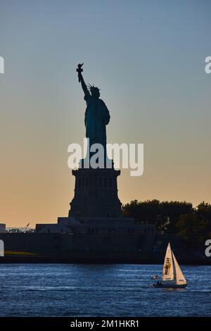 Silhouette de la Statue de la liberté avec un petit voilier qui passe à l'heure de la lumière et de l'or Banque D'Images
