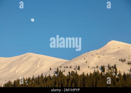 La lune dans le ciel bleu au-dessus des sommets blancs de montagne, loisirs dans la nature enneigée Banque D'Images