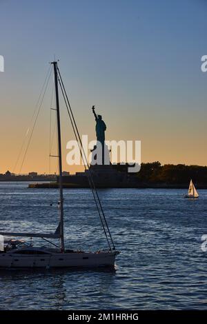 Silhouette de l'heure d'or de la Statue de la liberté avec des bateaux passant de l'eau Banque D'Images